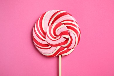 Photo of Stick with colorful lollipop swirl on pink background, top view