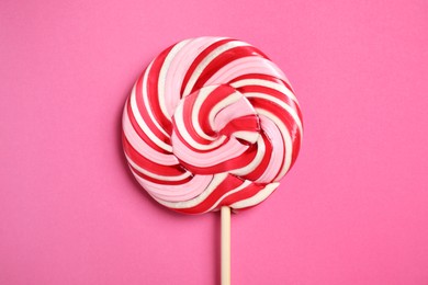 Stick with colorful lollipop swirl on pink background, top view