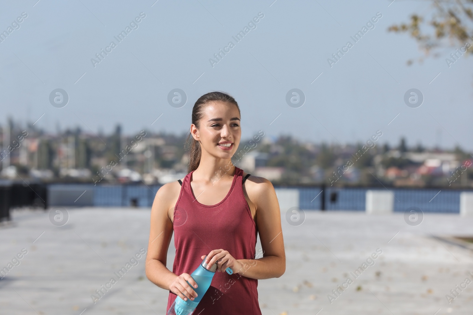 Photo of Young sporty woman holding bottle of water outdoors on sunny day