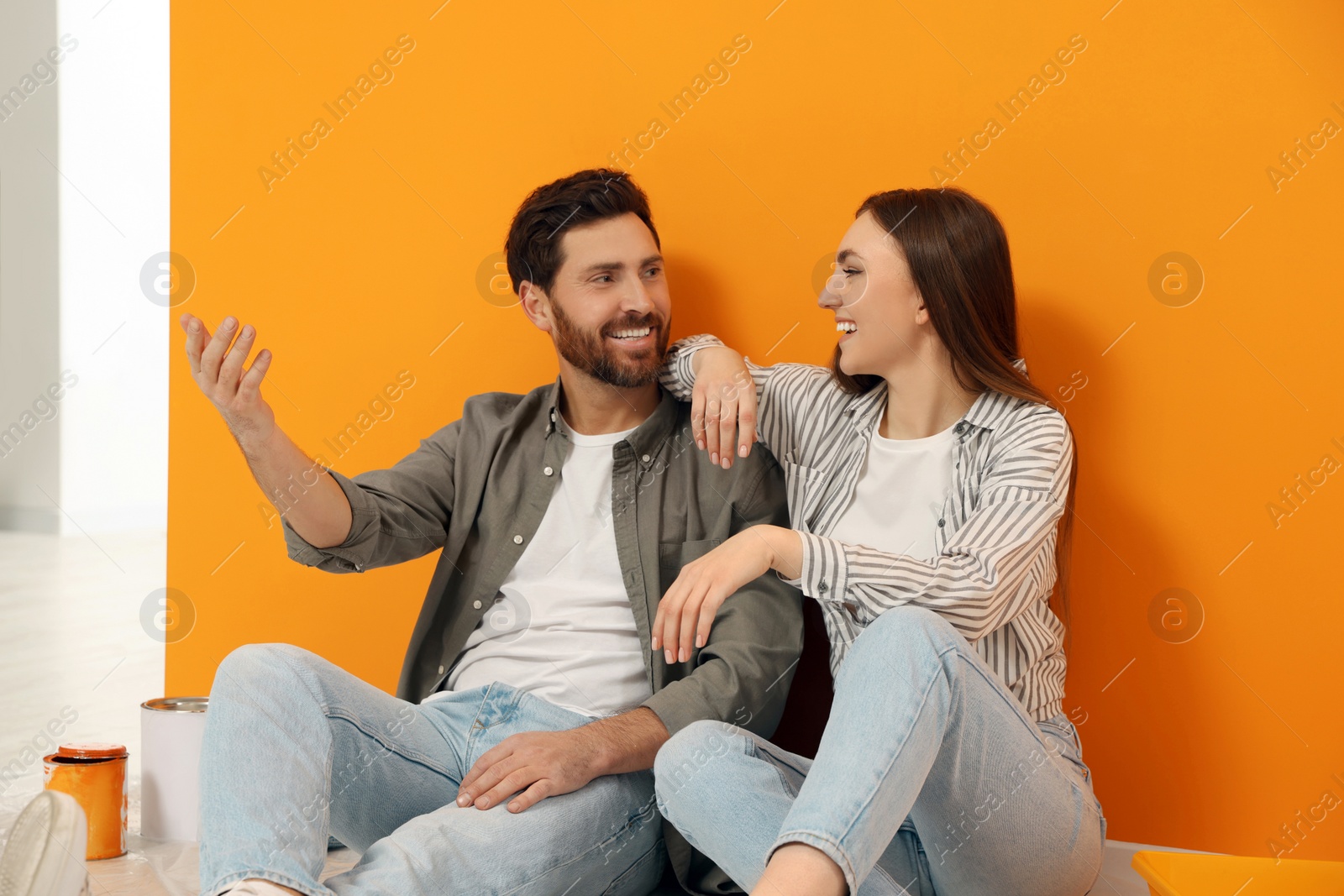 Photo of Happy designers sitting on floor near freshly painted orange wall