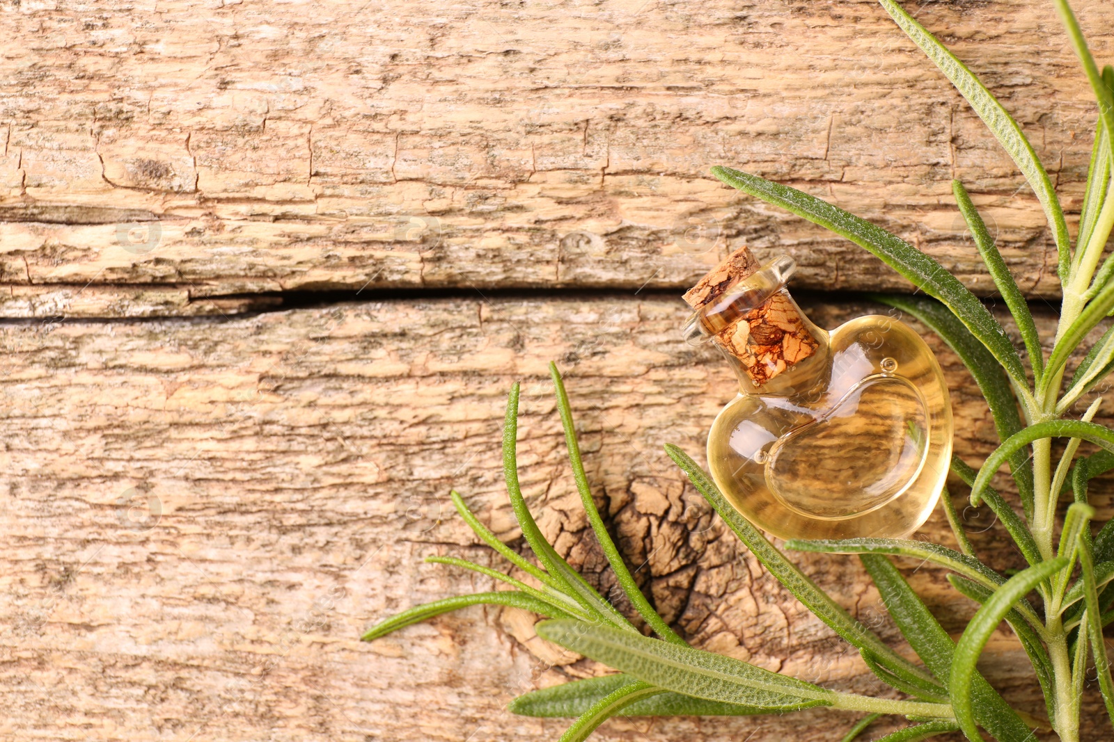 Photo of Aromatic essential oil in bottle and rosemary on wooden table, flat lay. Space for text