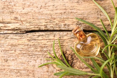 Aromatic essential oil in bottle and rosemary on wooden table, flat lay. Space for text