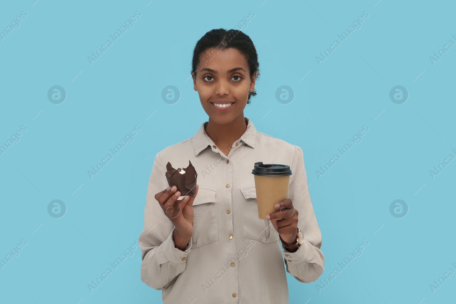 Photo of African American intern with cupcake and cup of drink on light blue background
