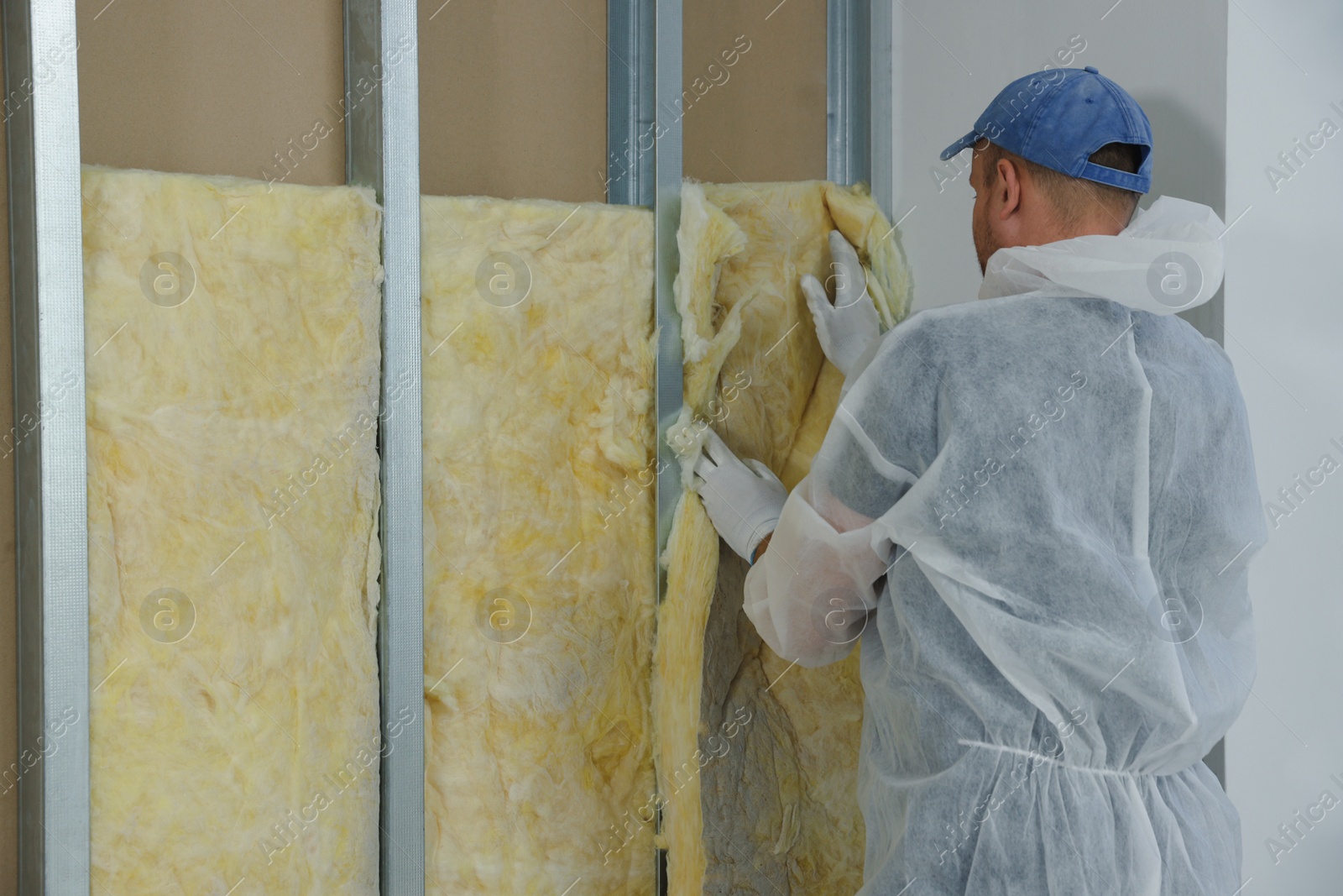 Photo of Worker insulating wall indoors, back view. Space for text