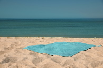 Turquoise beach towel on sand near sea, space for text