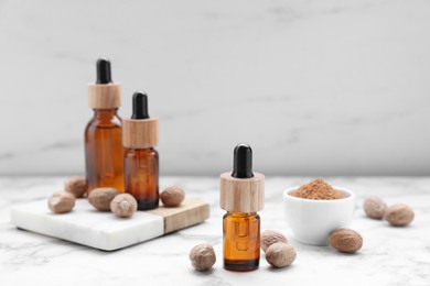 Bottles of nutmeg oil and nuts on white marble table
