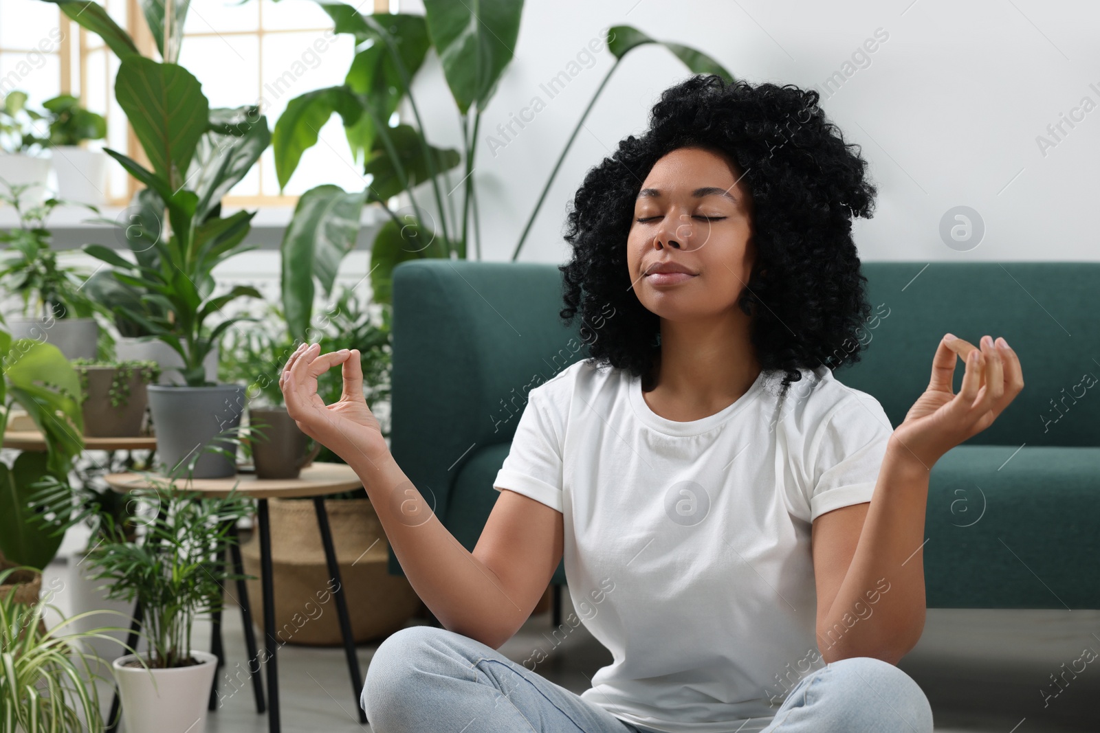 Photo of Relaxing atmosphere. Woman meditating near potted houseplants in room