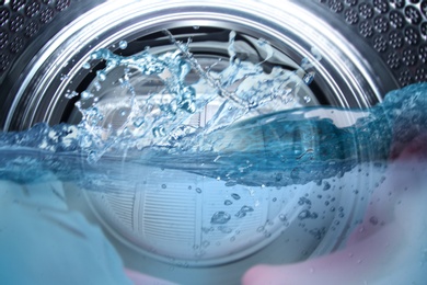Image of Washing machine drum with water and clothes, closeup view