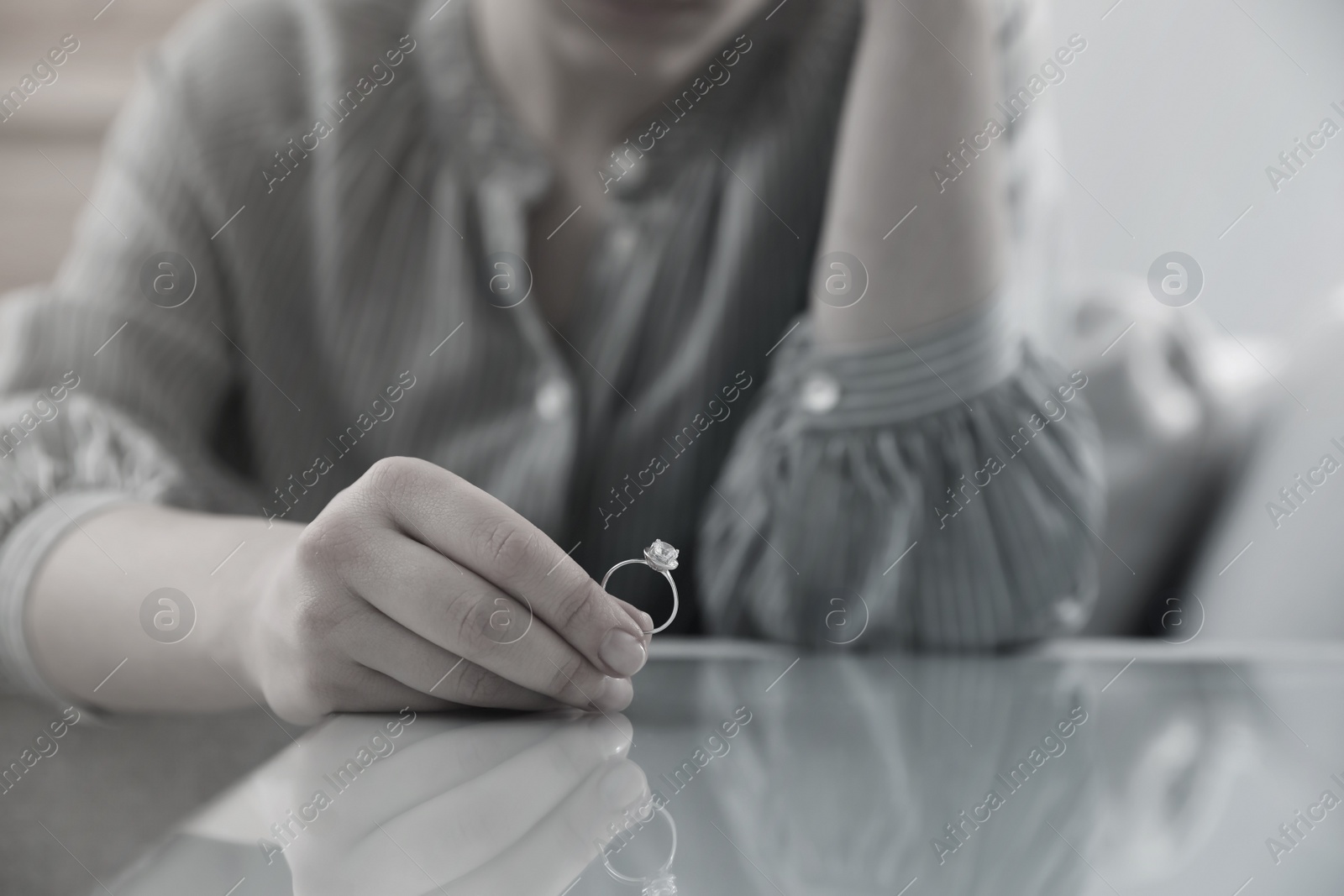 Image of Woman holding wedding ring at table indoors, closeup. Cheating and breakup