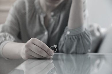 Woman holding wedding ring at table indoors, closeup. Cheating and breakup