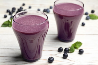 Tasty acai drink in glasses and berries on white wooden table, closeup