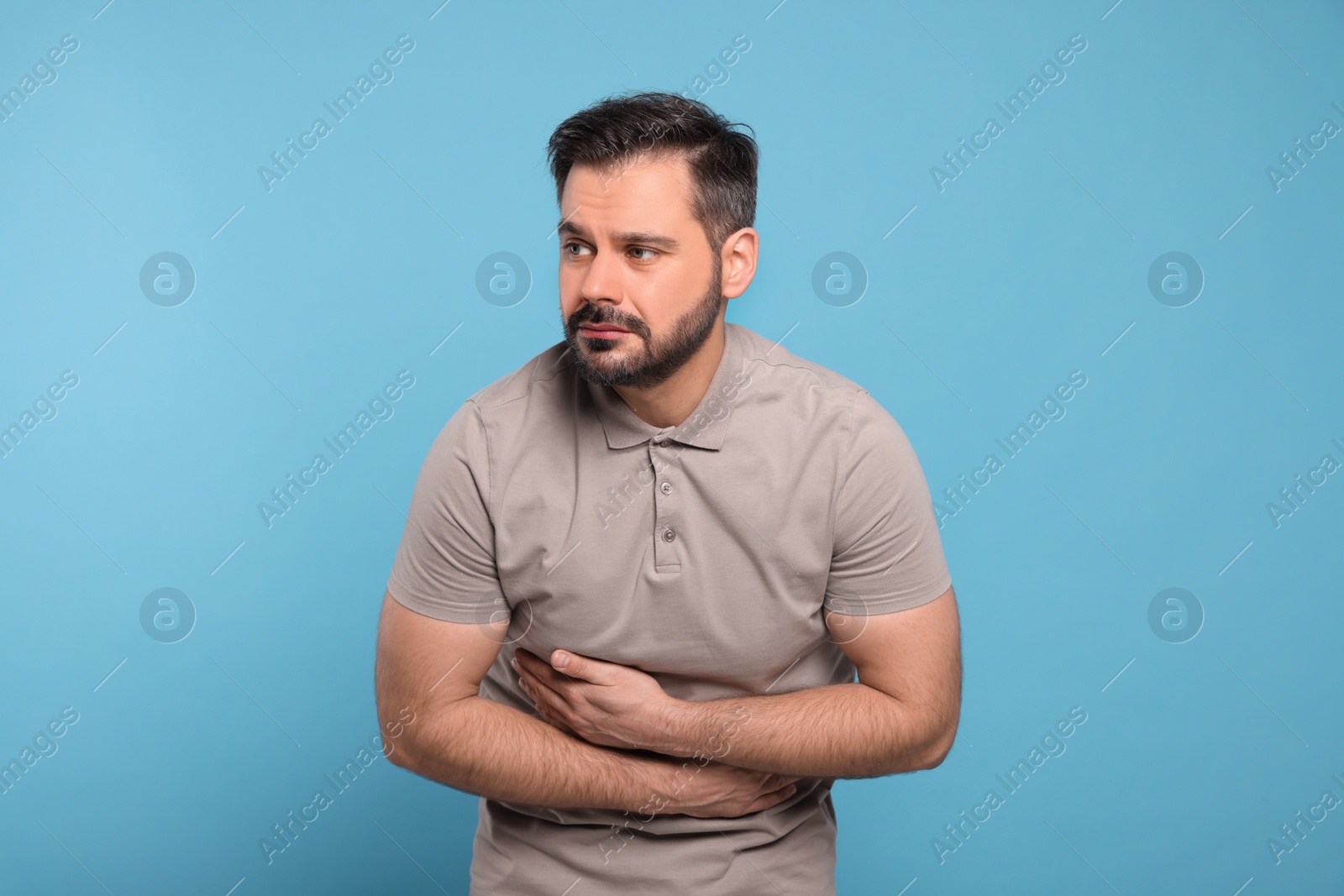 Photo of Unhappy man suffering from stomach pain on light blue background