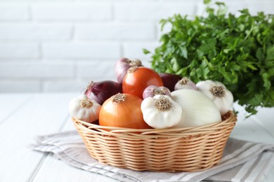 Photo of Fresh raw garlic and onions in wicker basket on white table