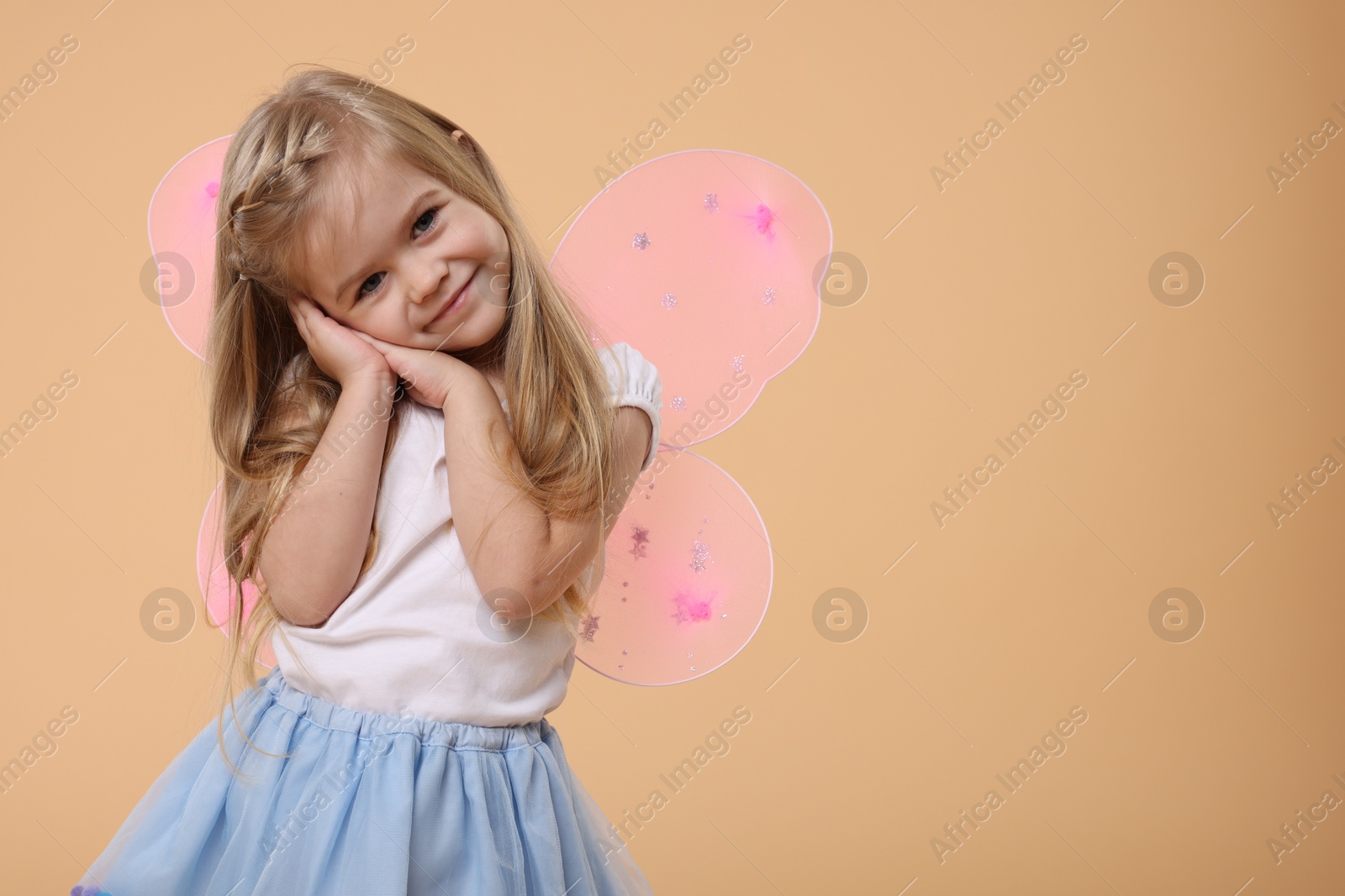 Photo of Cute little girl in fairy costume with pink wings on beige background, space for text