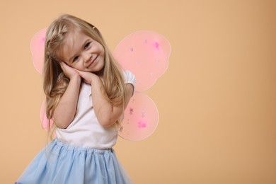 Cute little girl in fairy costume with pink wings on beige background, space for text