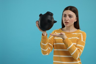 Sad woman with piggy bank on light blue background, space for text