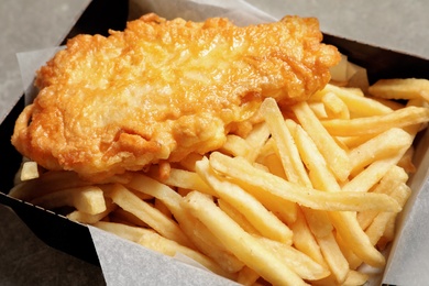 Photo of Disposable container with British Traditional Fish and potato chips on grey background