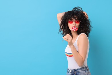 Photo of Beautiful woman in sunglasses with lollipop on light blue background, space for text