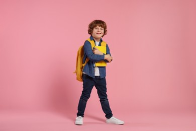 Happy schoolboy with backpack and books on pink background