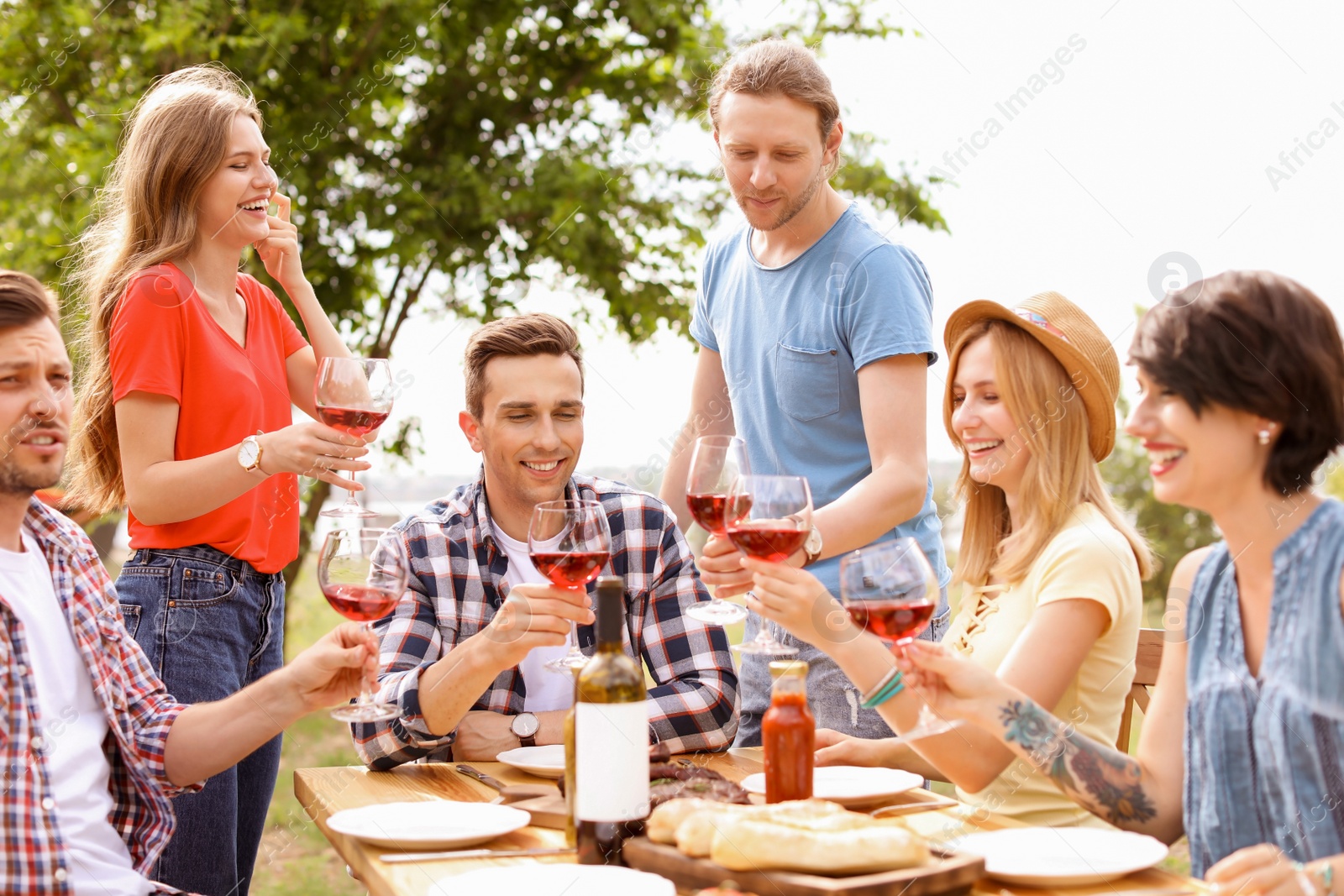 Photo of Young people with glasses of wine at table outdoors. Summer barbecue