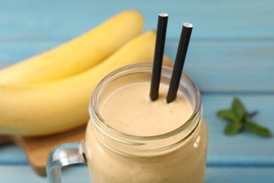 Photo of Mason jar with banana smoothie on light blue wooden table, closeup