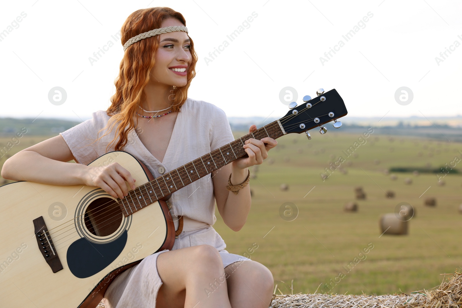 Photo of Beautiful hippie woman playing guitar on hay bale in field