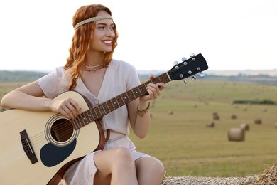 Beautiful hippie woman playing guitar on hay bale in field
