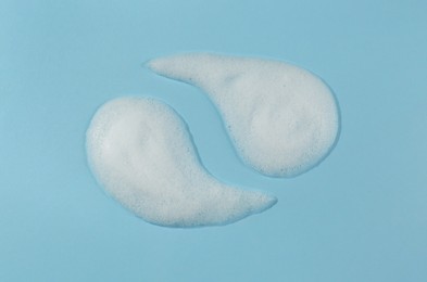 Photo of Samples of cleansing foam on light blue background, above view. Cosmetic product