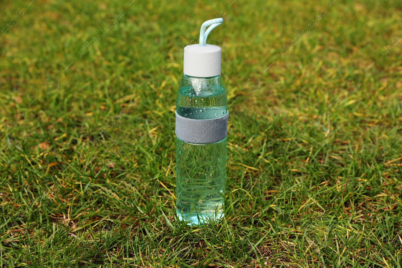 Photo of Glass bottle of fresh water on green grass outdoors