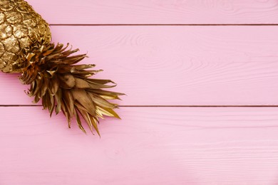 Golden pineapple on pink wooden table, top view. Space for text