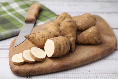Photo of Whole and cut turnip rooted chervil tubers on light wooden table, closeup