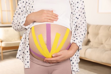 Photo of Pregnant woman with kinesio tapes on her belly at home, closeup