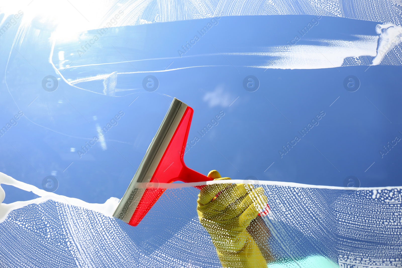 Photo of Woman cleaning glass with squeegee on sunny day, closeup