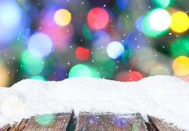 Image of Wooden surface with heap of snow and blurred Christmas lights on background, bokeh effect 