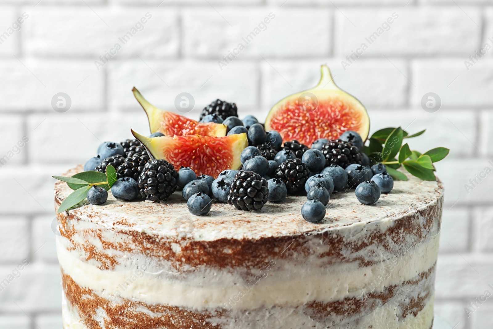 Photo of Delicious homemade cake with fresh berries near brick wall, closeup