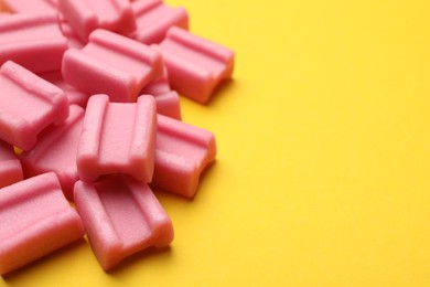 Photo of Tasty pink chewing gums on yellow background, closeup. Space for text