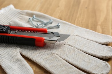 Photo of Utility knife, screws and glove on wooden table, closeup