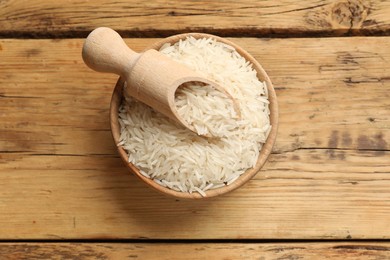 Photo of Raw basmati rice in bowl and scoop on wooden table, top view