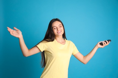 Happy young woman with air conditioner remote control on light blue background