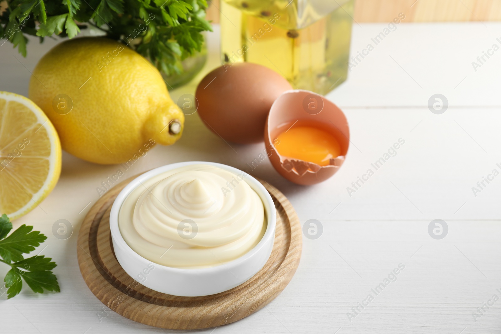 Photo of Fresh mayonnaise sauce in bowl and ingredients on white wooden table, space for text