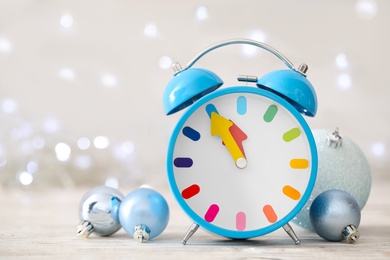 Photo of Alarm clock with decor on white wooden table against blurred Christmas lights, closeup. New Year countdown