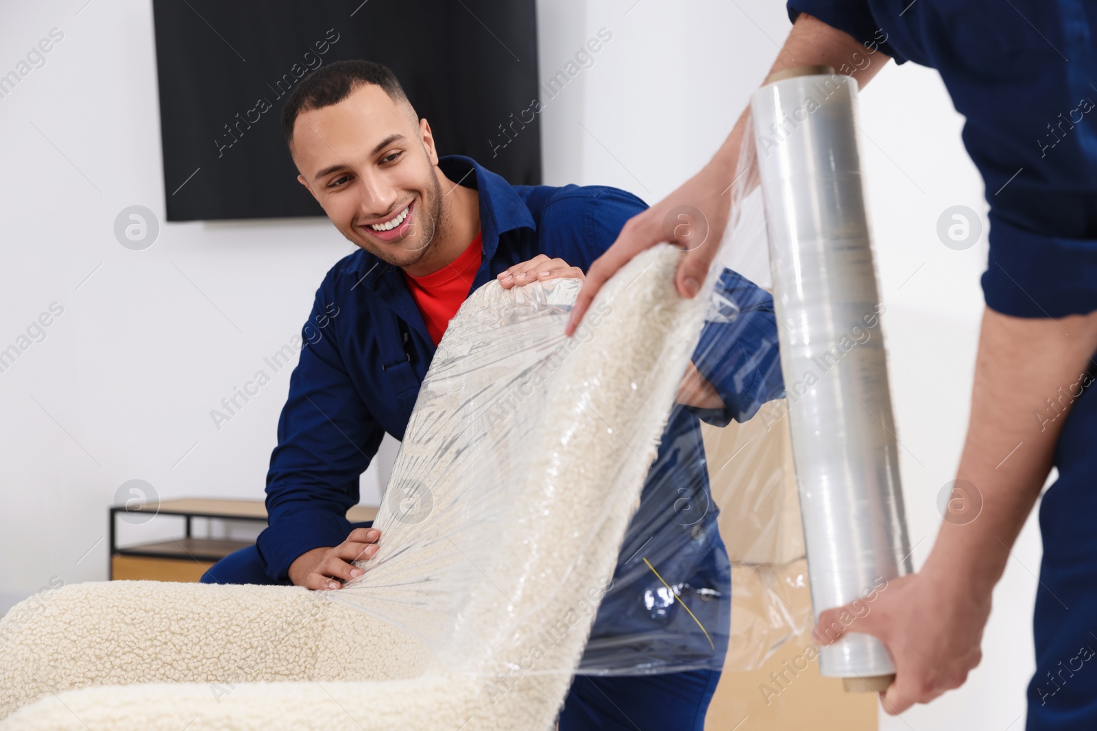 Photo of Male movers with stretch film wrapping armchair in house