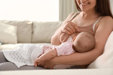 Photo of Young woman breastfeeding her little baby on sofa at home, closeup