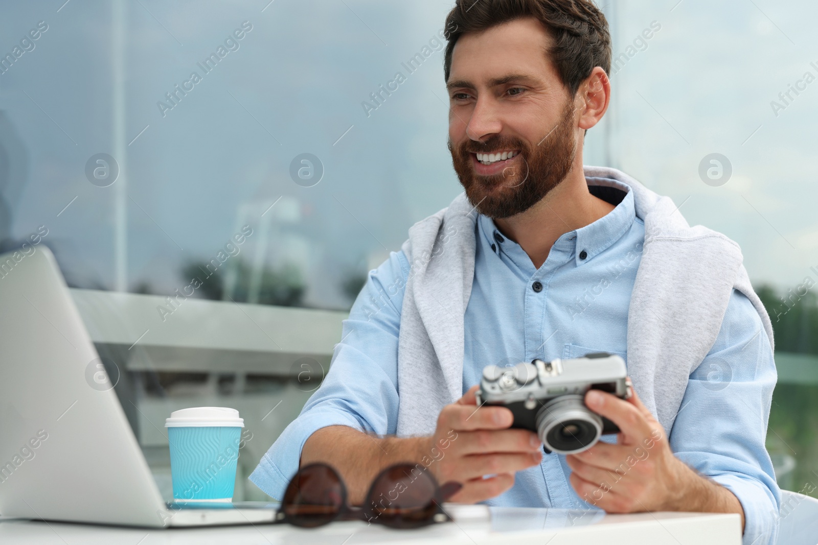 Photo of Man with camera, coffee and laptop in outdoor cafe. Interesting hobby