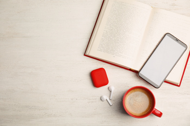 Book, coffee, earphones and mobile phone on white wooden table, flat lay. Space for text