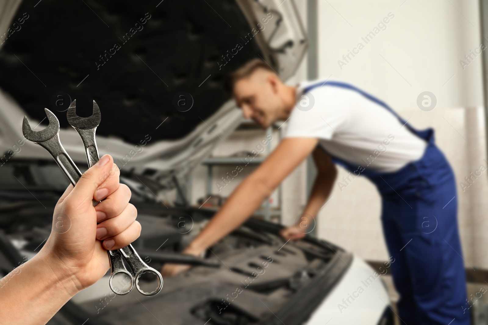 Image of Auto mechanic with wrenches near broken down car in repair shop, closeup