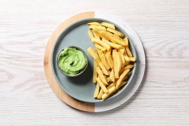Tray with plate of french fries, salt and avocado dip on white wooden table, top view