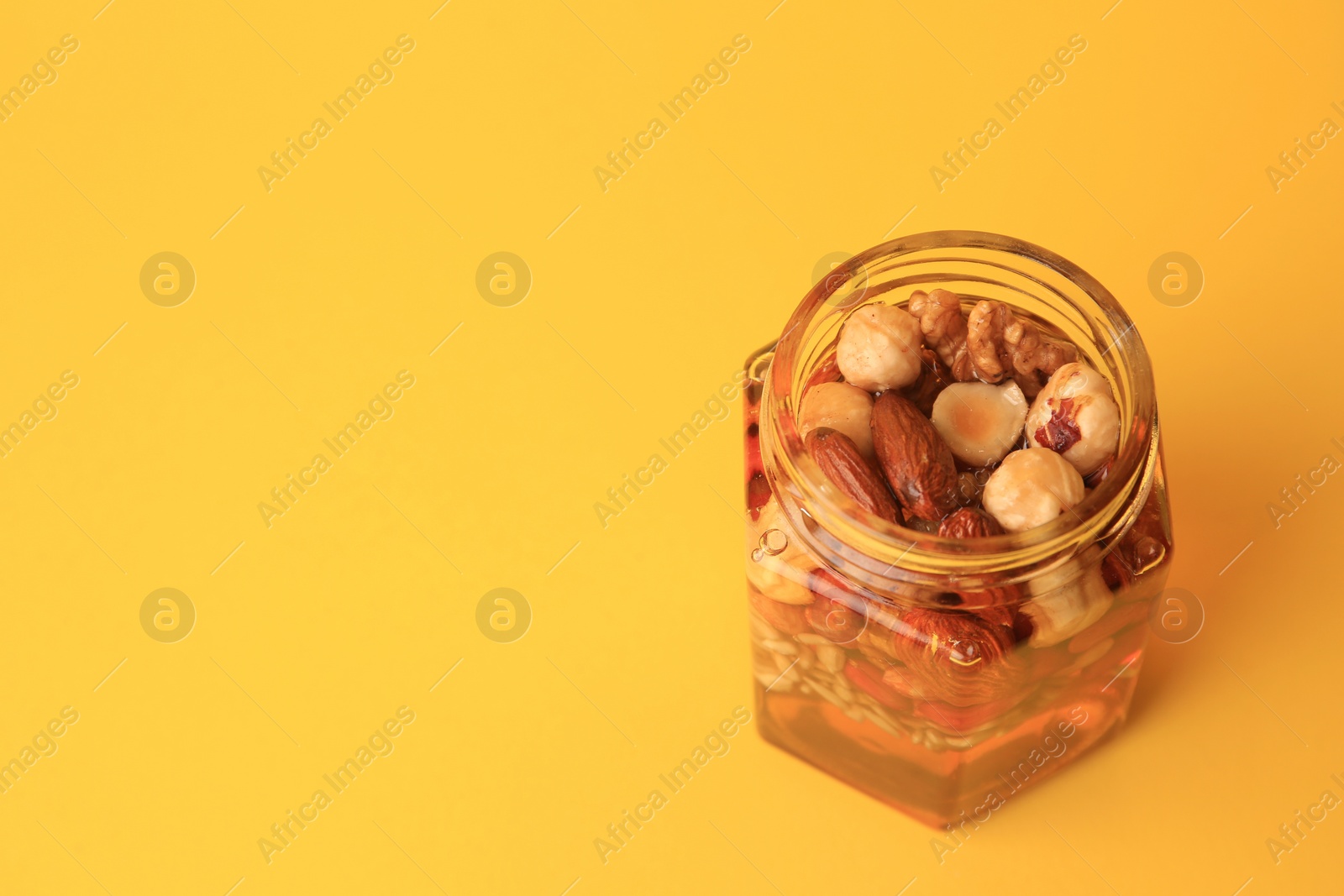 Photo of Different nuts and honey in jar on yellow background, above view. Space for text