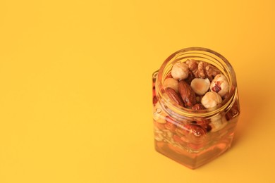 Different nuts and honey in jar on yellow background, above view. Space for text