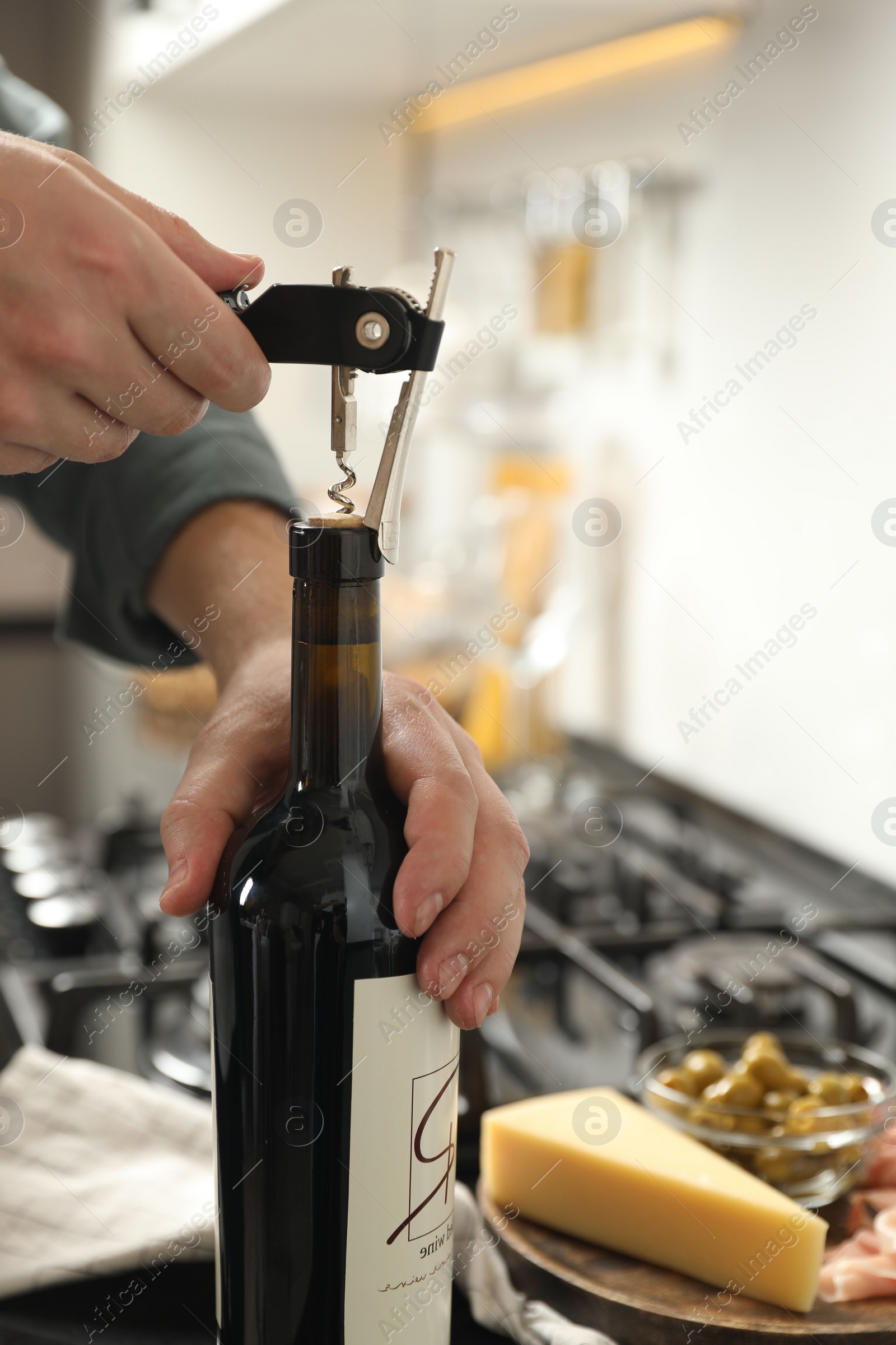 Photo of Man opening wine bottle with corkscrew indoors, closeup